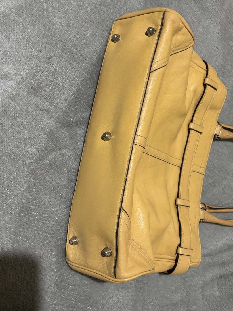 Coach Leather Tote Bag Yellow Tan (Category: Luxury Bags & Wallets) located in Taguig. Submitted by wonyjg (Listing ID 1466161531, Image 2). Description: Coach yellow leather tote bag with silver tone hardware and buckle strap detail across the front. Dual shoulder straps, protective metal feet on the bottom. Interior fabric lining includes a zippered pocket and slip pockets. Coach creed patch stamped inside with serial number. Classic structured