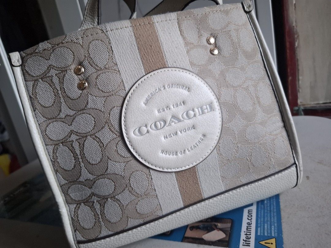 Coach Signature Canvas Tote Bag (Category: Luxury Bags & Wallets) located in Marikina City. Submitted by bags21.ph (Listing ID 1466336757, Image 1). Description: - Authentic Coach signature jacquard canvas tote - Elegant cream leather trim and gold-tone hardware - Classic Coach New York round leather patch with vertical stripe - Structured design with protective metal feet on the bottom - Dual top carry handles and side rings for strap attachment