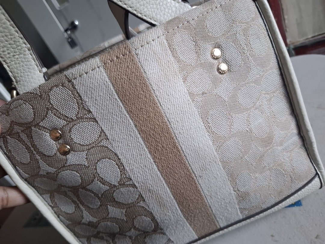 Coach Signature Canvas Tote Bag (Category: Luxury Bags & Wallets) located in Marikina City. Submitted by bags21.ph (Listing ID 1466336757, Image 2). Description: - Authentic Coach signature jacquard canvas tote - Elegant cream leather trim and gold-tone hardware - Classic Coach New York round leather patch with vertical stripe - Structured design with protective metal feet on the bottom - Dual top carry handles and side rings for strap attachment