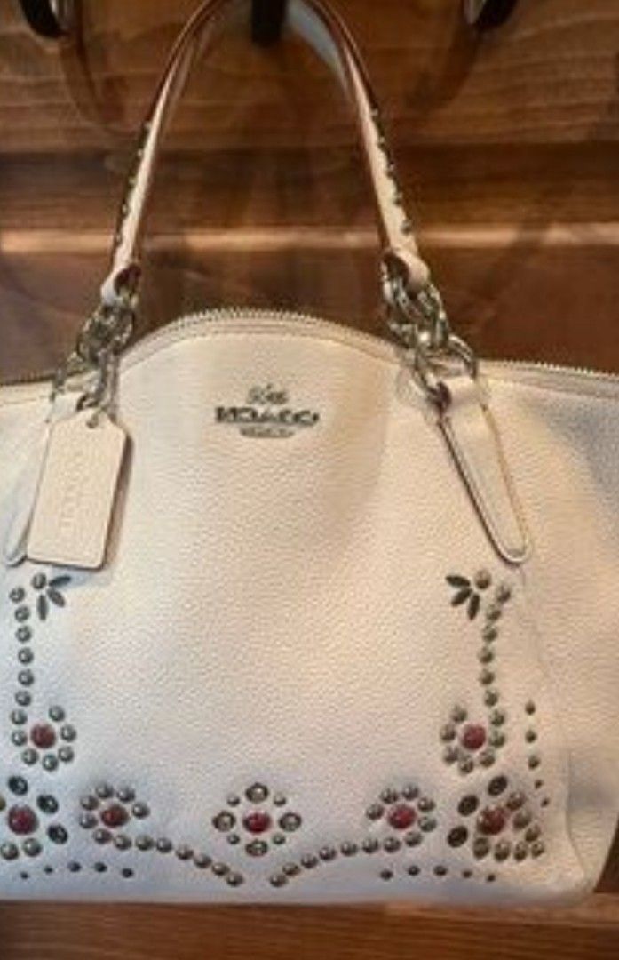 Coach White Leather Studded Handbag with Shoulder Strap (Category: Cross-body Bags) located in Manila. Submitted by lene48 (Listing ID 1466242461, Image 1). Description: - Brand: Coach - Material: White pebbled leather with silver-tone hardware - Design: Gorgeous floral studded and gemstone embellishments on the front, featuring the Coach horse and carriage logo - Handles & Strap: Dual rolled top handles with contrasting burgundy edging and a mat