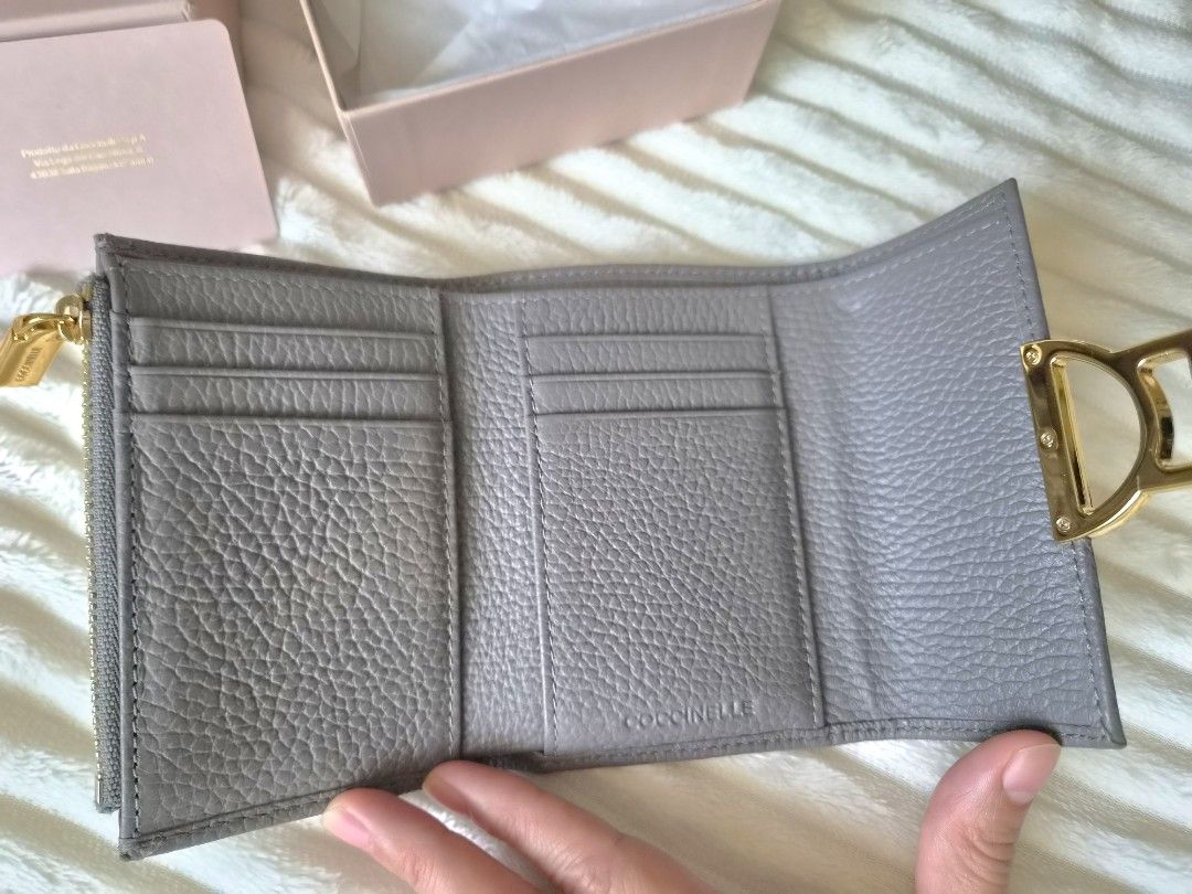 Coccinelle Trifold Leather Wallet with Box (Category: Wallets & Card holders) located in Paranaque City. Submitted by sampgm (Listing ID 1466208850, Image 3). Description: - Brand: Coccinelle - Material: Premium grey pebbled leather - Hardware: Gold-tone with signature clasp closure - Interior: Multiple card slots and secure zippered pocket - Inclusions: Original pink branded box and card - Condition: Well-maintained, minor scratches on hardware 