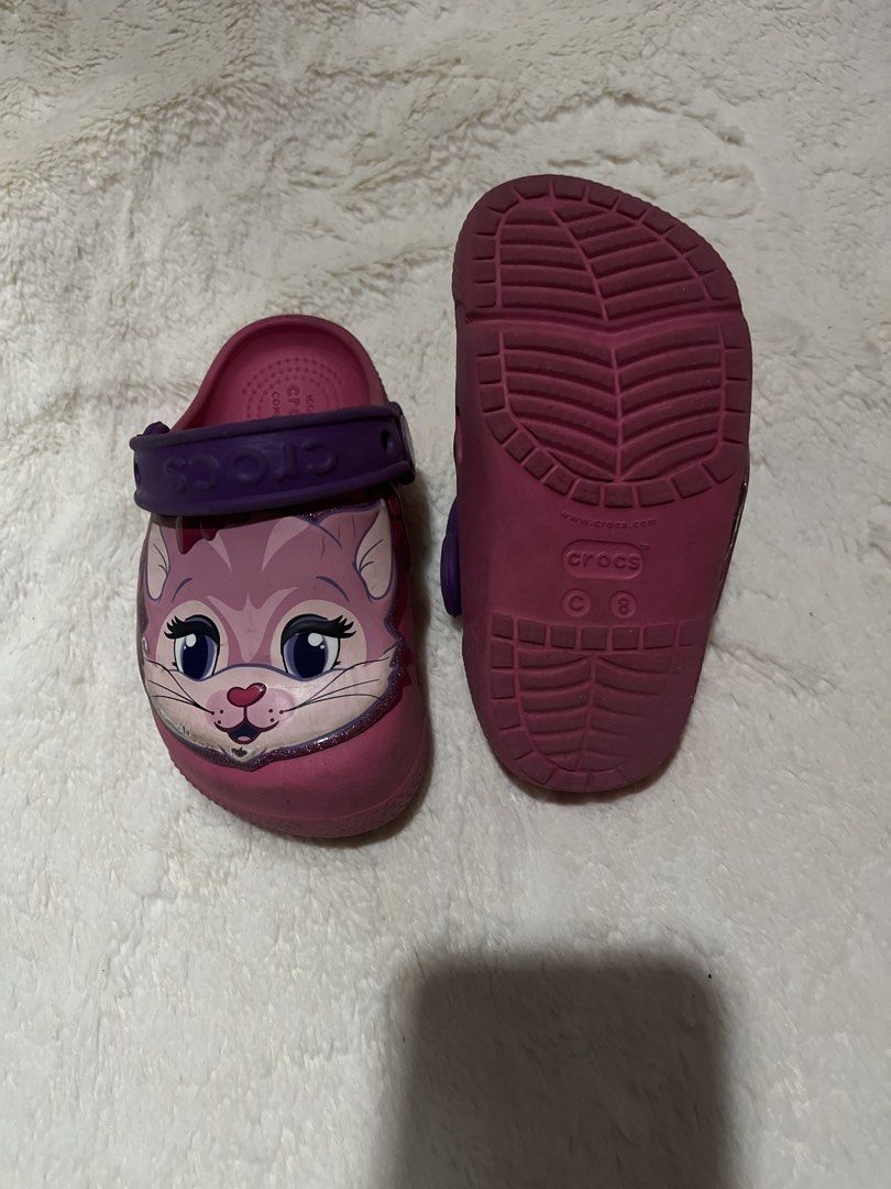 Crocs Kids Light Up Cat Clogs Size C8 (Category: Babies & Kids Fashion) located in Carmona. Submitted by abimeng08 (Listing ID 1466302404, Image 2). Description: - Color: Pink with purple heel straps - Size: C8 (stamped on sole) - Design: Cute cat graphic with big eyes and whiskers - Special Feature: One shoe lights up near the nose - Style: Slip-on, perfect for toddlers - Condition: Normal signs of wear on soles and sides.