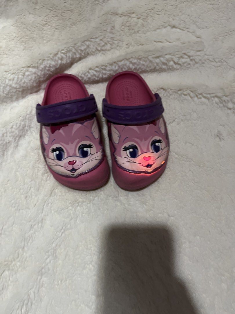 Crocs Kids Light Up Cat Clogs Size C8 (Category: Babies & Kids Fashion) located in Carmona. Submitted by abimeng08 (Listing ID 1466302404, Image 3). Description: - Color: Pink with purple heel straps - Size: C8 (stamped on sole) - Design: Cute cat graphic with big eyes and whiskers - Special Feature: One shoe lights up near the nose - Style: Slip-on, perfect for toddlers - Condition: Normal signs of wear on soles and sides.