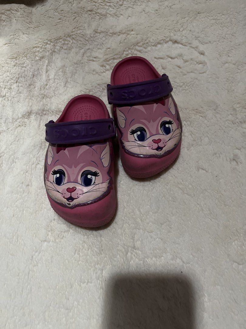 Crocs Kids Light Up Cat Clogs Size C8 (Category: Babies & Kids Fashion) located in Carmona. Submitted by abimeng08 (Listing ID 1466302404, Image 1). Description: - Color: Pink with purple heel straps - Size: C8 (stamped on sole) - Design: Cute cat graphic with big eyes and whiskers - Special Feature: One shoe lights up near the nose - Style: Slip-on, perfect for toddlers - Condition: Normal signs of wear on soles and sides.