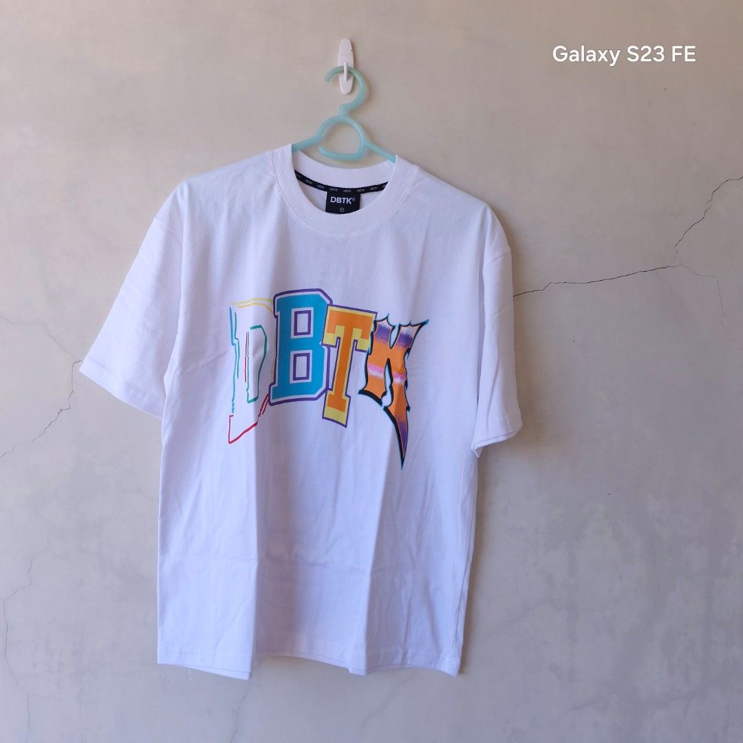 DBTK Graphic Tee White (Category: Tshirts & Polo Shirts ) located in Iloilo. Submitted by franzventures (Listing ID 1466179043, Image 1). Description: - Brand: DBTK (Don't Blame The Kids) - Color: Clean White - Design: Large front chest logo with a vibrant, detailed streetwear art and skull collage on the back - Fit: Short sleeves, crew neck - Style: Must-have streetwear piece.