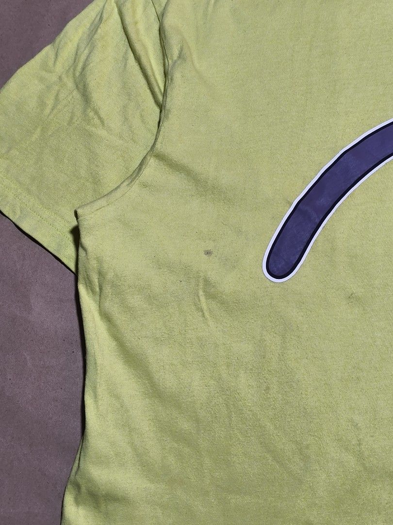 Evisu Lime Green Graphic T-Shirt (Category: Tshirts & Polo Shirts ) located in Manila. Submitted by thriftclothin (Listing ID 1466301726, Image 2). Description: - Brand: Evisu - Color: Bright lime green with a large purple graphic logo - Features: Short sleeves, crew neck, small branded black tag at the hem, Korean inner wash tag with QR code - Condition: Minor fabric wear and a faint stain near the lower left front graphic - Authentic streetwear