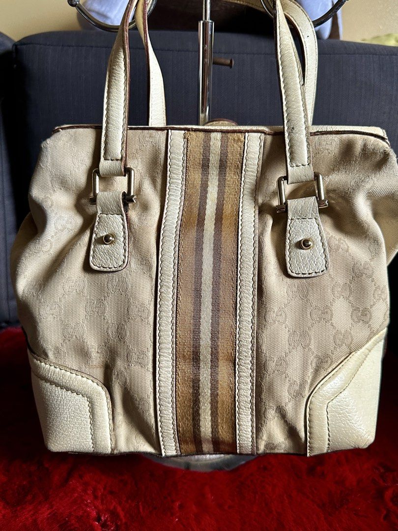 Gucci GG Canvas Web Stripe Padlock Tote Handbag (Category: Luxury Bags & Wallets) located in Quezon City. Submitted by shopaholic.kart2021 (Listing ID 1466228575, Image 2). Description: Beige and white Gucci handbag with GG monogram canvas and brown web stripe down the center. Silver-tone hardware includes a front lock closure with hanging key and chain detail. Cream leather trim and dual top handles. Interior features a zippered pocket and leath