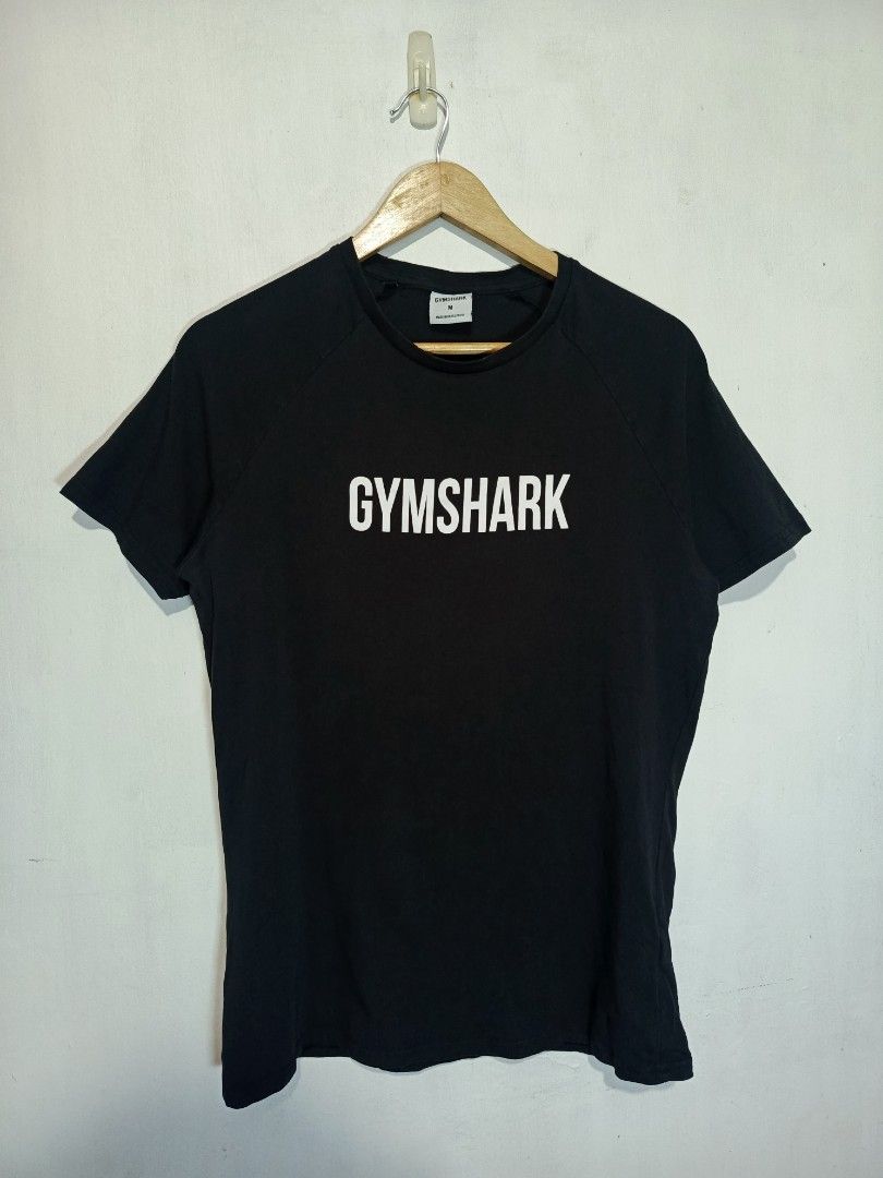 GYMSHARK SHIRT (Category: Tshirts & Polo Shirts ) located in Baguio. Submitted by 074thriftmania (Listing ID 1466254134, Image 1). Description: - Brand: Gymshark - Color: Black with bold white chest logo - Size: Men's Medium - Fit: Regular fit, short sleeves, crew neck - Material: Comfortable cotton blend (Made in Bangladesh) - Condition: Clean inner tags and clear wash care label attached - Ideal for: Gym workouts and casual daily wear.
