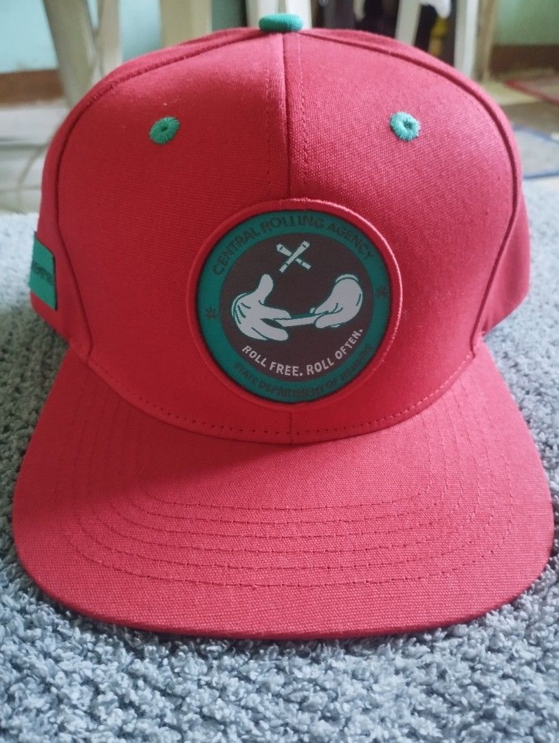 Hempire Snapback Cap Red Teal (Category: Caps & Hats) located in Manila. Submitted by happycaps (Listing ID 1466172127, Image 1). Description: - Brand: Hempire Alpine Headwear - Style: Red snapback cap with flat teal-undervisor brim - Front Details: Central Rolling Agency patch with rolling hands graphic and "roll free, roll often" text - Interior: All-over weed leaf pattern lining - Closure: Adjustable teal snap closure with small fabric tag - C
