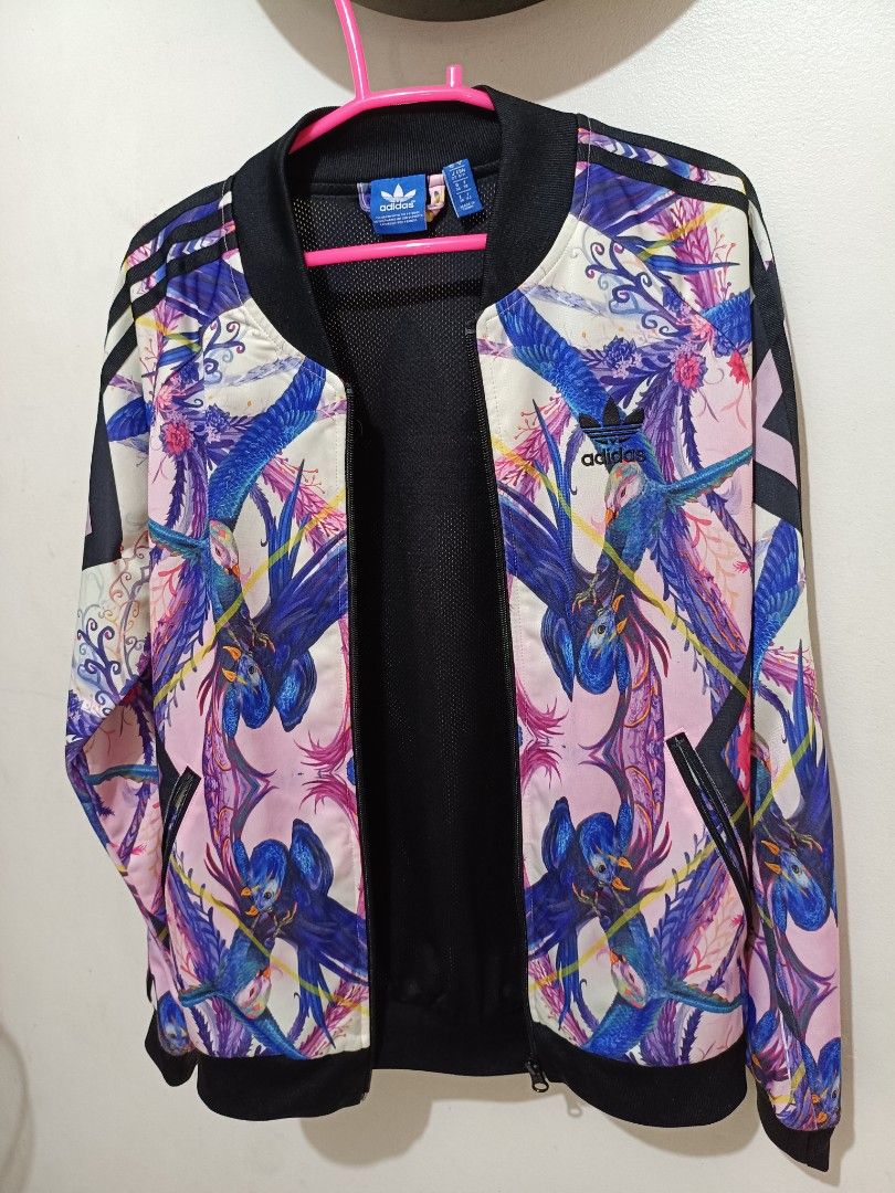 superstar track jacket (Category: Activewear) located in Limay. Submitted by lisa_2318 (Listing ID 1466169853, Image 3). Description: Features an all-over tropical print mixing vibrant pinks, purples, and blues, showcasing abstract floral details and exotic birds. Authentic Adidas originals teack jacket from the "Florera"/optic bloom collection..