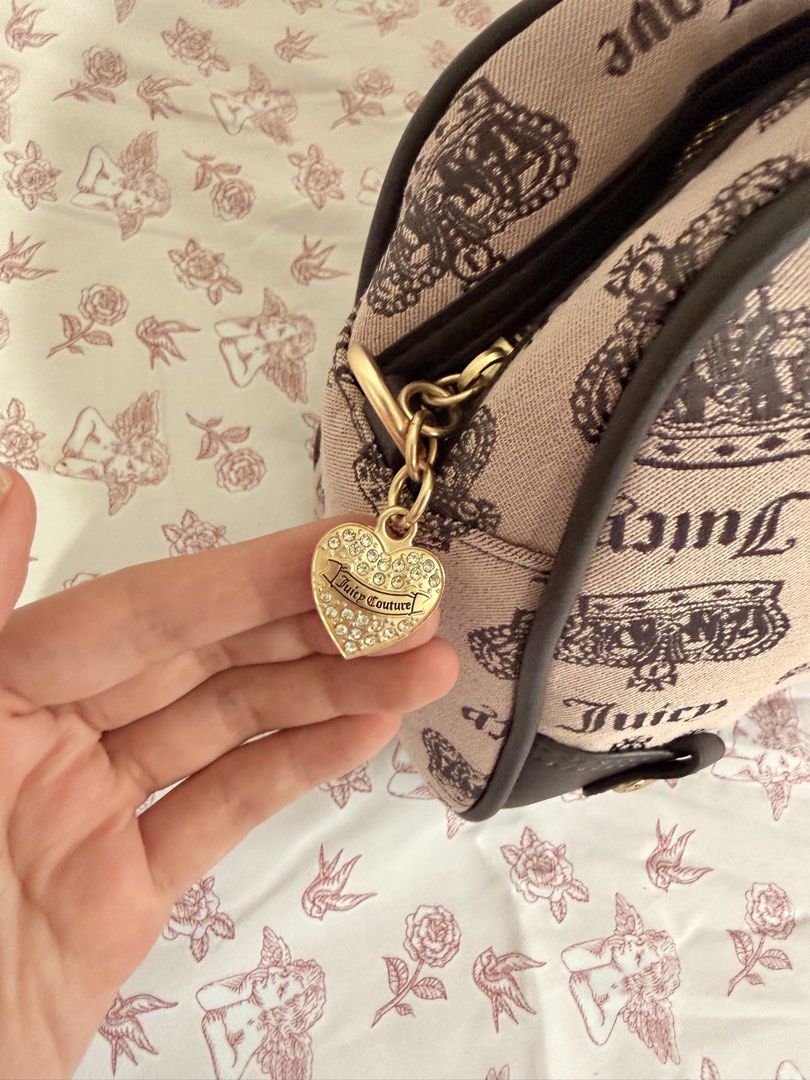 Juicy Couture Monogram Boston Handbag with Bow Charm (Category: Luxury Bags & Wallets) located in Cebu City. Submitted by katvictoria (Listing ID 1466298965, Image 3). Description: - Brand: Juicy Couture - Style: Barrel handbag - Color/Design: Pink fabric with black crown and logo print, accented with dark brown trim - Hardware: Gold-tone hardware with front metal logo plate - Charms: Includes a gold bow charm with heart-shaped tag and a rhinesto