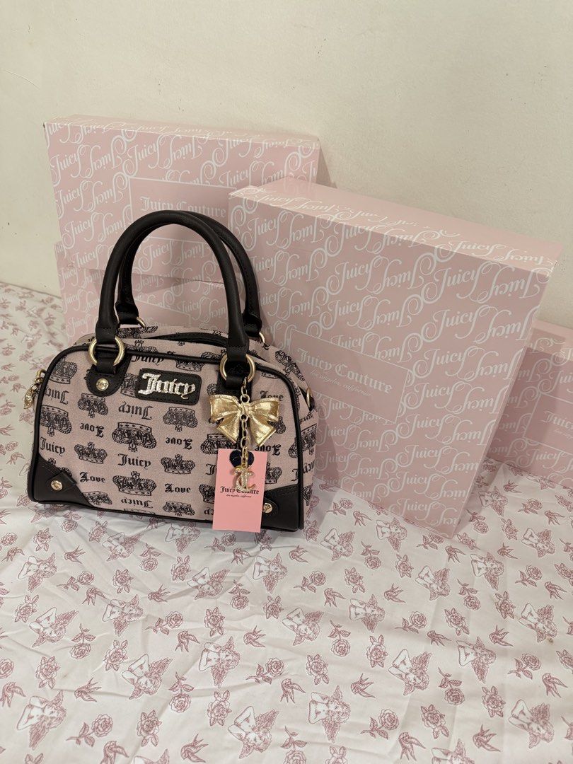 Juicy Couture Monogram Boston Handbag with Bow Charm (Category: Luxury Bags & Wallets) located in Cebu City. Submitted by katvictoria (Listing ID 1466298965, Image 2). Description: - Brand: Juicy Couture - Style: Barrel handbag - Color/Design: Pink fabric with black crown and logo print, accented with dark brown trim - Hardware: Gold-tone hardware with front metal logo plate - Charms: Includes a gold bow charm with heart-shaped tag and a rhinesto