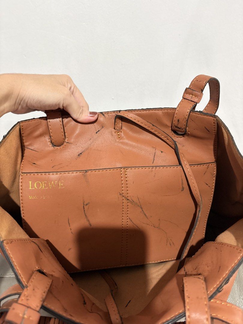 Loewe Brown Leather Tote Bag (Category: Tote Bags) located in Mandaluyong City. Submitted by gentle.segoviajam (Listing ID 1466262525, Image 3). Description: Tan brown leather tote bag by Loewe. Made in Spain. Large debossed Anagram logo on the front. Double top handles and internal slip pocket with gold embossed branding. Interior shows heavy black scuff marks and ink stains throughout. Exterior leather has general wear..