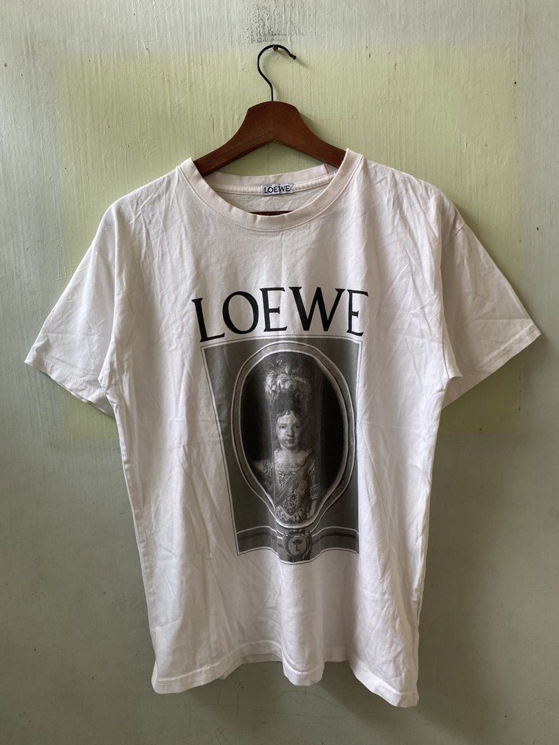 LOEWE Graphic Print White T-Shirt (Category: Shirts) located in Pandi. Submitted by nasya_thrift_collection2023 (Listing ID 1466198210, Image 1). Description: - Brand: Loewe - Color: White - Design: Front framed portrait graphic with bold lettering, signature Anagram logo printed near the back collar - Cut: Standard crew neck and short sleeves - Condition: Clean, interior brand tag and care label intact - Styling: Versatile, easy to pair with jea