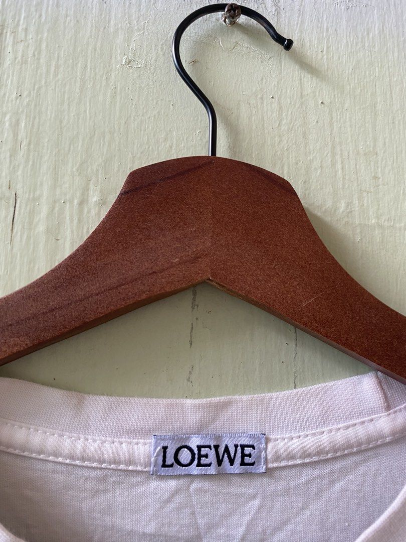 LOEWE Graphic Print White T-Shirt (Category: Shirts) located in Pandi. Submitted by nasya_thrift_collection2023 (Listing ID 1466198210, Image 3). Description: - Brand: Loewe - Color: White - Design: Front framed portrait graphic with bold lettering, signature Anagram logo printed near the back collar - Cut: Standard crew neck and short sleeves - Condition: Clean, interior brand tag and care label intact - Styling: Versatile, easy to pair with jea
