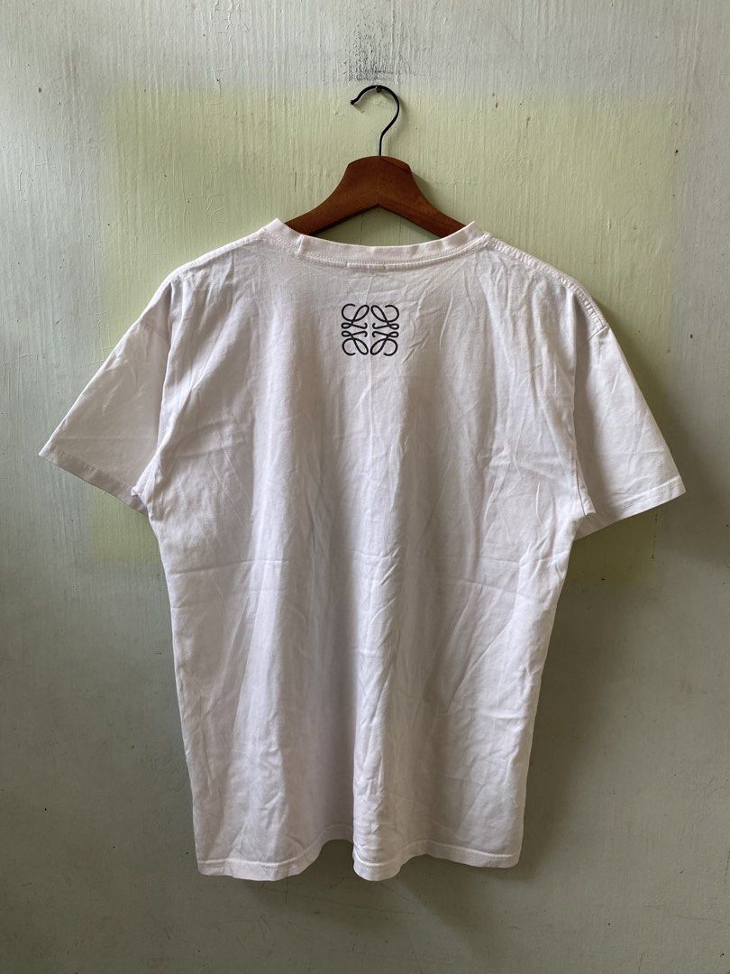 LOEWE Graphic Print White T-Shirt (Category: Shirts) located in Pandi. Submitted by nasya_thrift_collection2023 (Listing ID 1466198210, Image 2). Description: - Brand: Loewe - Color: White - Design: Front framed portrait graphic with bold lettering, signature Anagram logo printed near the back collar - Cut: Standard crew neck and short sleeves - Condition: Clean, interior brand tag and care label intact - Styling: Versatile, easy to pair with jea