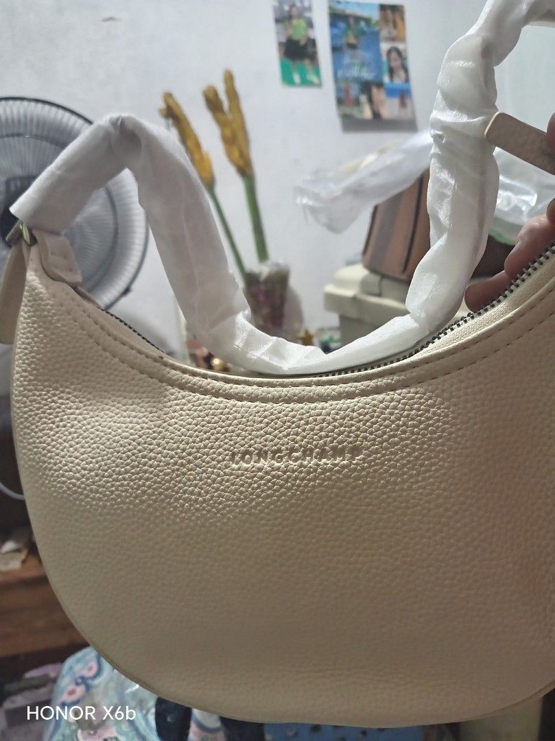 Longchamp Roseau Shoulder Bag Cream (Category: Luxury Bags & Wallets) located in Manila. Submitted by tuesdaymari (Listing ID 1466250471, Image 1). Description: - Brand: Longchamp - Color: Cream - Style: Curved crescent shoulder bag - Material: Textured leather with embossed front logo - Closure: Top zipper - Condition: Brand new, handles still wrapped in original protective white paper packaging - Features: Clean exterior, modern everyday design