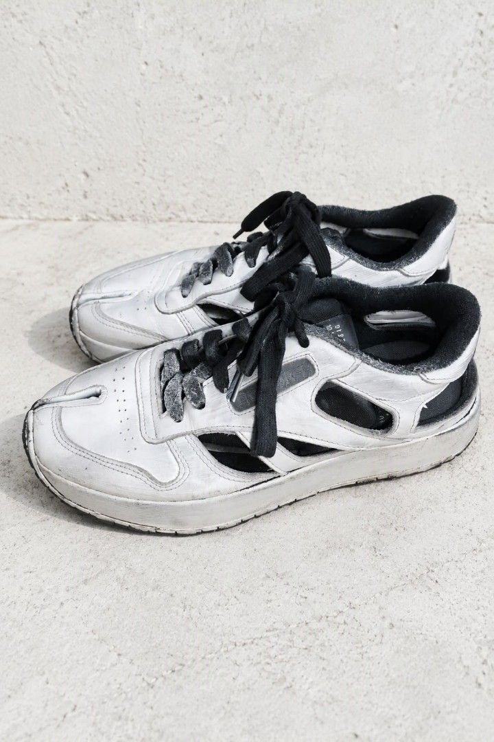 Maison Margiela x Reebok (Category: Sneakers) located in Baguio. Submitted by luxeloomarchive (Listing ID 1466173619, Image 2). Description: Maison Margiela x Reebok ​Description: Iconic Maison Margiela x Reebok Project 0 CL Tabi Decortique Low-Top Sneakers. Features Margiela's signature split Tabi toe design, 'Decortique' cut-out side paneling, hand-painted distressed white finish over a black base, lace-up closure, and dual branding on the tong