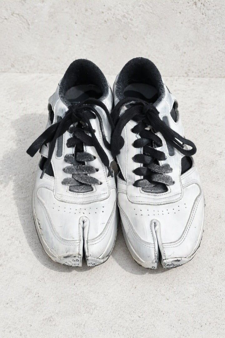 Maison Margiela x Reebok (Category: Sneakers) located in Baguio. Submitted by luxeloomarchive (Listing ID 1466173619, Image 1). Description: Maison Margiela x Reebok ​Description: Iconic Maison Margiela x Reebok Project 0 CL Tabi Decortique Low-Top Sneakers. Features Margiela's signature split Tabi toe design, 'Decortique' cut-out side paneling, hand-painted distressed white finish over a black base, lace-up closure, and dual branding on the tong