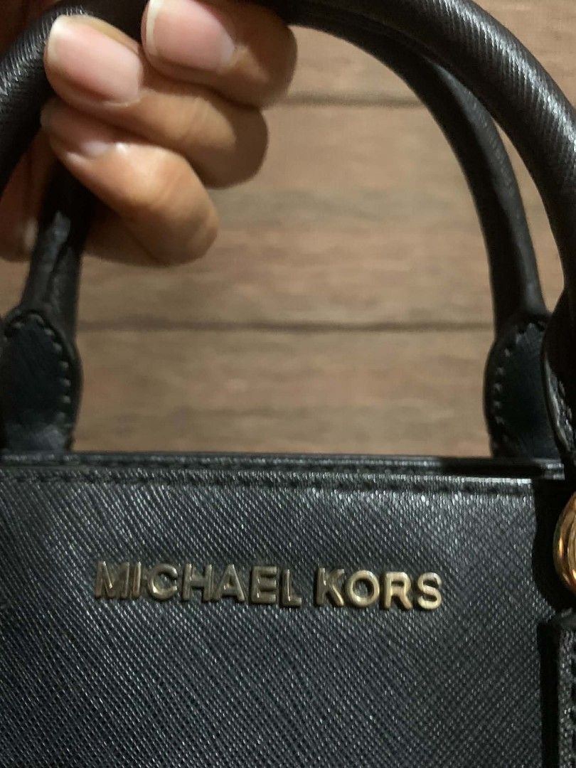 Michael Kors Black Studded Leather Handbag (Category: Luxury Bags & Wallets) located in Aliaga. Submitted by akishaoshop2010. (Listing ID 1466204051, Image 3). Description: - Brand: Michael Kors - Material: Premium black saffiano leather - Hardware: Gold-tone, featuring chic metal studs along the front - Design: Structured trapezoid shape with signature gold logo lettering - Straps: Double top handles plus a detachable, adjustable shoulder strap 