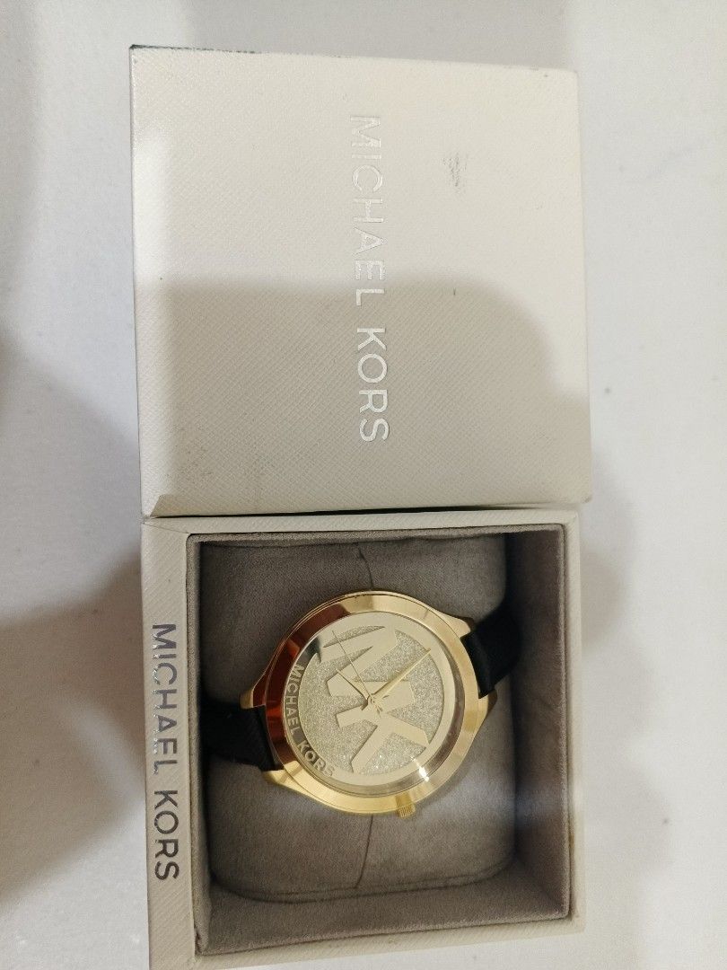 Michael Kors Gold Watch with Black Strap (Category: Women's Watches) located in Bacoor. Submitted by stardys8888 (Listing ID 1466288843, Image 1). Description: - Brand: Michael Kors - Design: Gold-tone case, large MK logo, and glamorous glitter background - Strap: Classic black leather strap - Inclusions: Original branded white box and gray watch pillow - Condition: Clean overall condition with minimal signs of handling on the box - Note: Battery