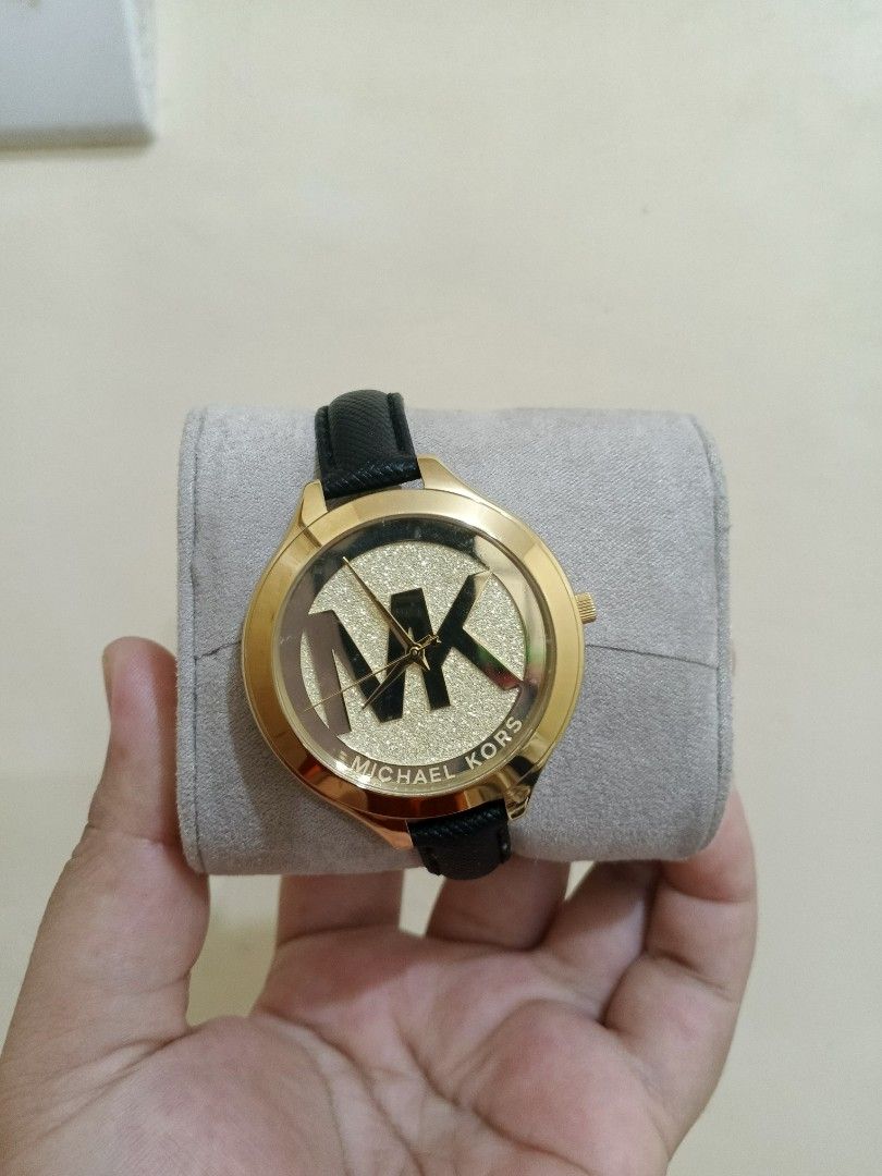 Michael Kors Gold Watch with Black Strap (Category: Women's Watches) located in Bacoor. Submitted by stardys8888 (Listing ID 1466288843, Image 2). Description: - Brand: Michael Kors - Design: Gold-tone case, large MK logo, and glamorous glitter background - Strap: Classic black leather strap - Inclusions: Original branded white box and gray watch pillow - Condition: Clean overall condition with minimal signs of handling on the box - Note: Battery