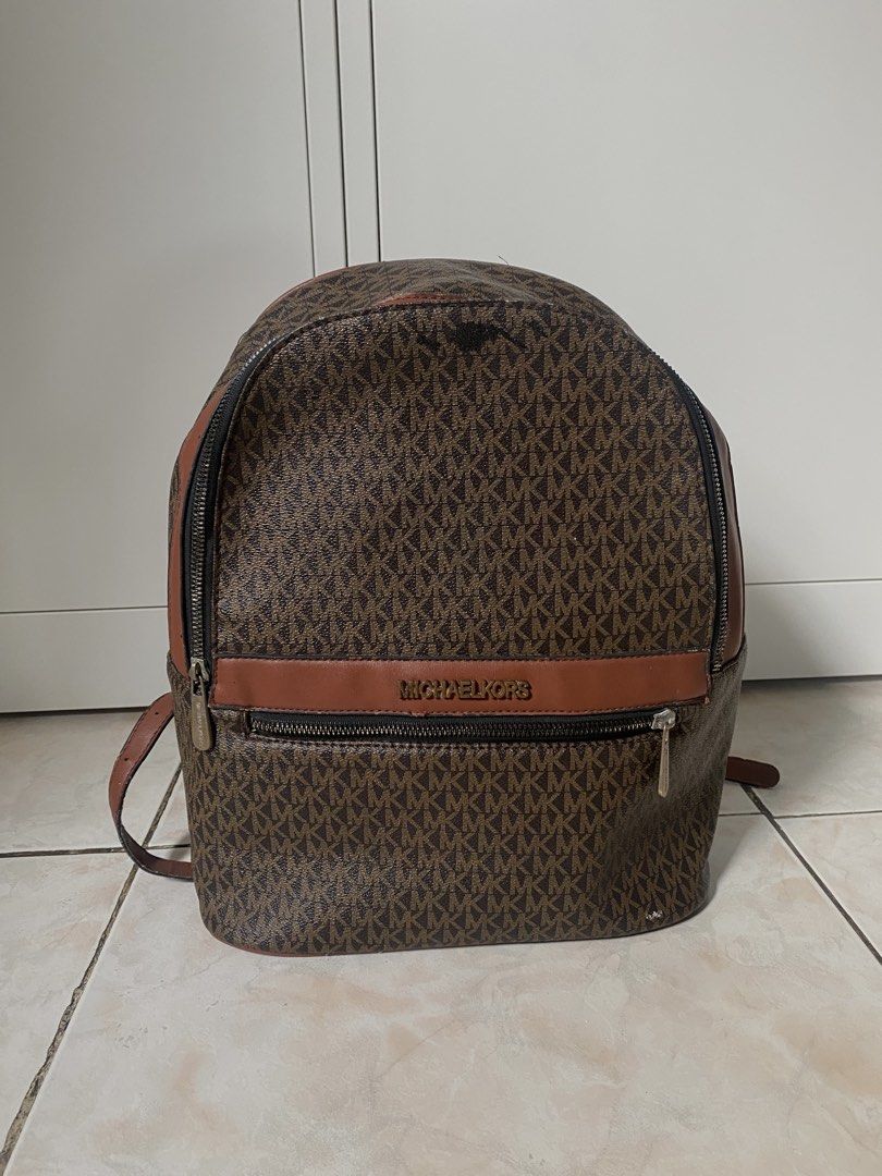 Michael Kors MK Monogram Brown Leather Backpack (Category: Backpacks) located in Marikina City. Submitted by makeitmorepretty (Listing ID 1466162697, Image 1). Description: Brown Michael Kors backpack featuring the iconic MK monogram pattern throughout. Accented with smooth brown leather trim and gold-tone hardware. Front zip pocket with Michael Kors lettering logo plaque. Top zip closure and adjustable shoulder straps. Roomy interior compartment