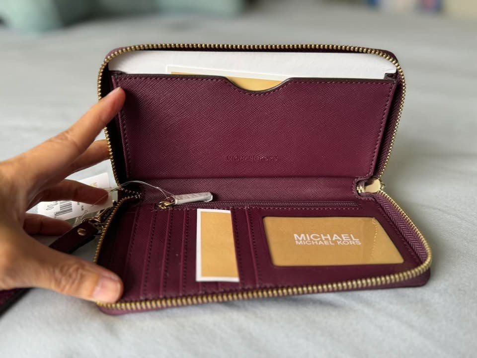 Michael Kors Plum Leather Wristlet Wallet (Category: Wallets & Card holders) located in Manila. Submitted by flojo1220 (Listing ID 1466211226, Image 2). Description: Plum purple leather wallet from Michael Kors. Gold-tone hardware with the circular MK logo on the front. Zip-around closure keeps everything secure. Inside has multiple card slots, slip compartments, and a zippered coin pocket. Clear ID window on one side. Brand tags still attached. 