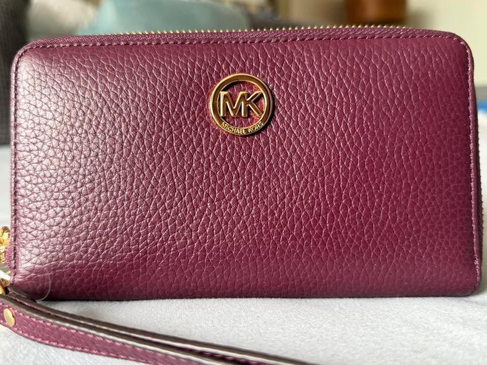 Michael Kors Plum Leather Wristlet Wallet (Category: Wallets & Card holders) located in Manila. Submitted by flojo1220 (Listing ID 1466211226, Image 1). Description: Plum purple leather wallet from Michael Kors. Gold-tone hardware with the circular MK logo on the front. Zip-around closure keeps everything secure. Inside has multiple card slots, slip compartments, and a zippered coin pocket. Clear ID window on one side. Brand tags still attached. 