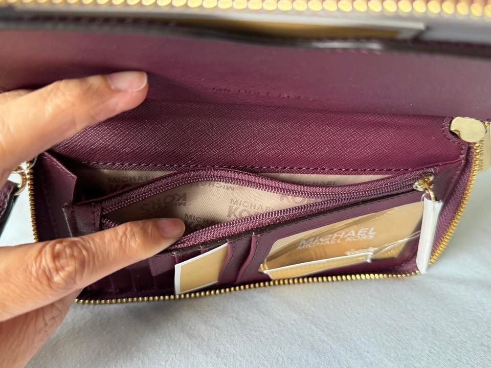 Michael Kors Plum Leather Wristlet Wallet (Category: Wallets & Card holders) located in Manila. Submitted by flojo1220 (Listing ID 1466211226, Image 3). Description: Plum purple leather wallet from Michael Kors. Gold-tone hardware with the circular MK logo on the front. Zip-around closure keeps everything secure. Inside has multiple card slots, slip compartments, and a zippered coin pocket. Clear ID window on one side. Brand tags still attached. 