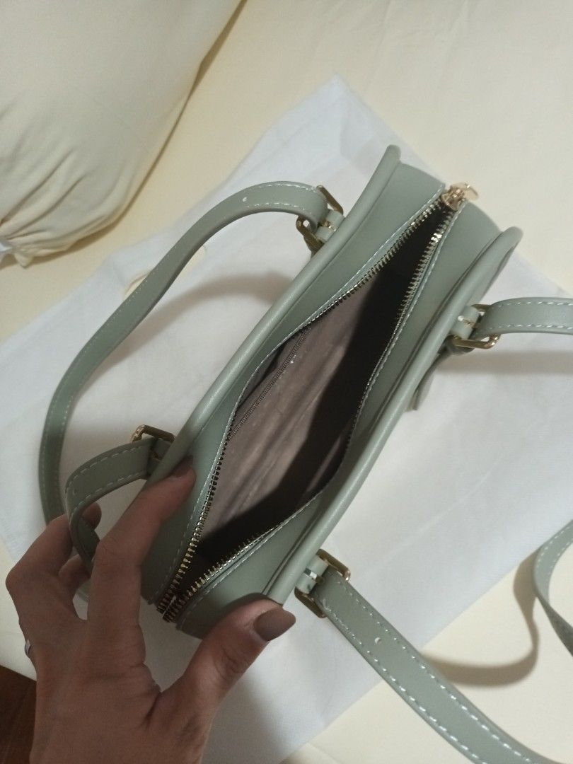Mossdoom Sage Green Shoulder Bag (Category: Shoulder Bags) located in Quezon. Submitted by ja8720 (Listing ID 1466242922, Image 3). Description: Mossdoom shoulder bag in sage green. Clean structured rectangular shape with contrast white stitching along the dual handles and straps. Gold-tone hardware details include front decorative buckle straps and a top zipper closure. Interior lined with fabric. Includes original white dust bag with Mossdoom l