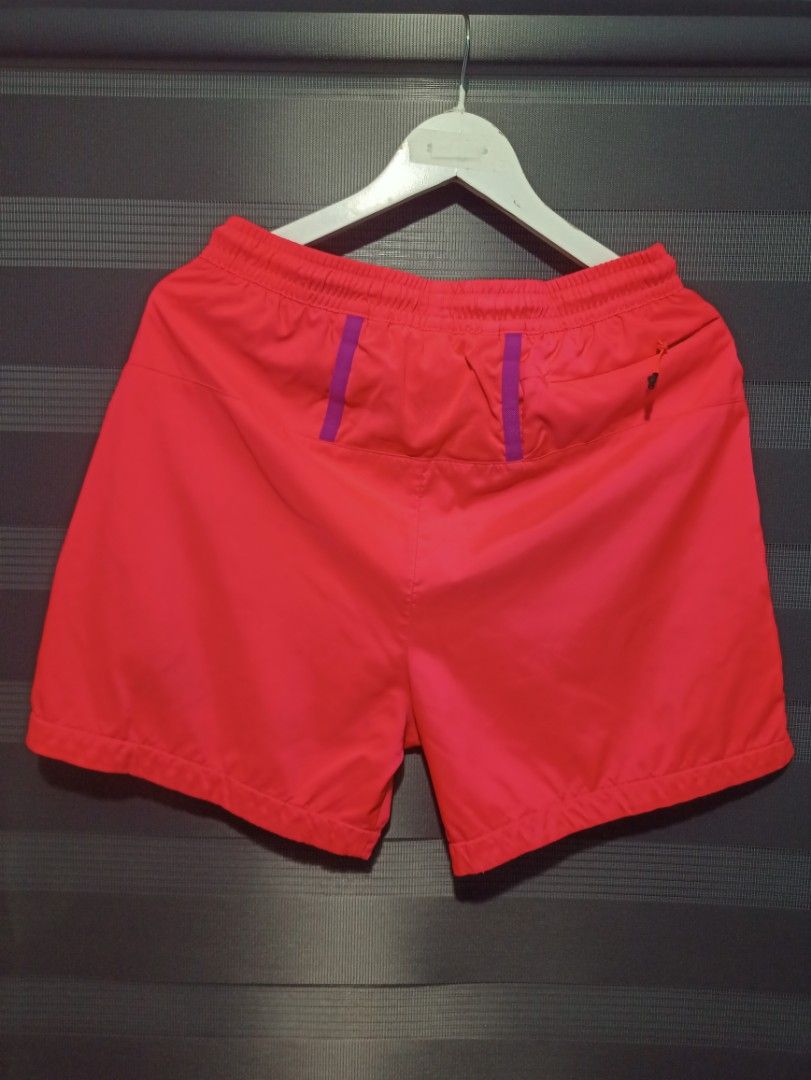 Nike ACG Pink Shorts Size M (Category: Activewear) located in Manila. Submitted by thecomftrift.co (Listing ID 1466324294, Image 2). Description: - Brand: Nike ACG - Color: Bright pink with orange and yellow accents - Size: Medium - Features: Elastic waistband, adjustable orange drawstrings, side zip pockets, rear zip pocket, and back waist loops - Details: Purple triangle logo on the lower left leg - Condition/Fit: Lightweight fabric; flat lay m