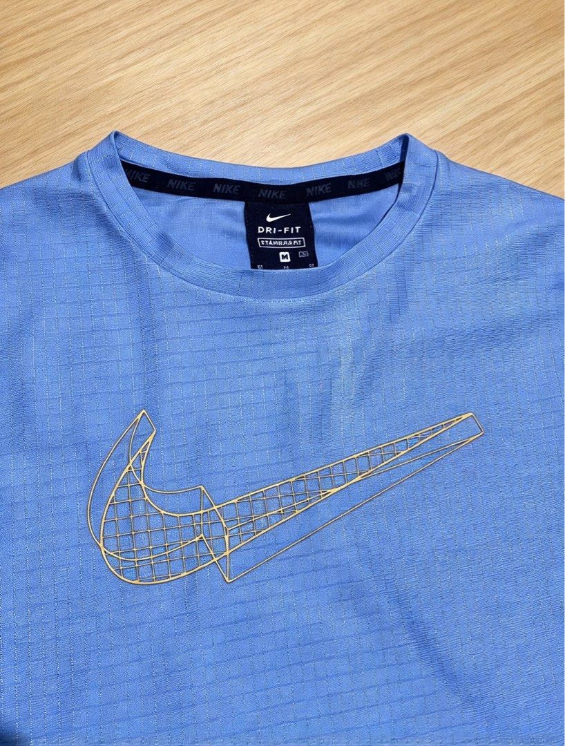 Nike Dri-FIT Graphic T-Shirt (Category: Activewear) located in Manila. Submitted by tygaangub1096 (Listing ID 1466291468, Image 2). Description: - Brand: Nike Dri-FIT - Size: Medium - Dimes: 16 width 23 length - Color: Light Blue - Design: Rare gold geometric net-style Swoosh graphic on the chest - Material: Grid-textured performance fabric for cooling and moisture management - Condition: Clean, no fading or damage - Authenticity: Style code DA02