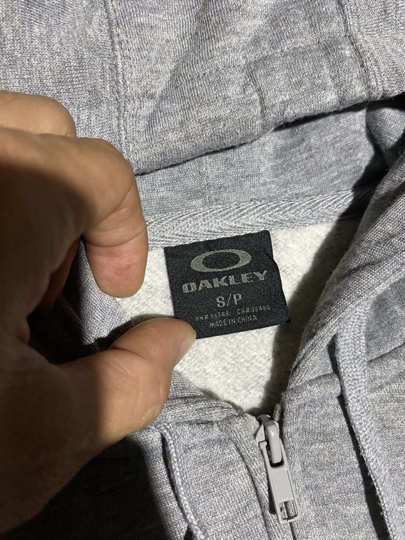 Oakley Grey Zip-Up Hoodie (Category: Coats, Jackets and Outerwear) located in Badiangan. Submitted by iralorana.thrift (Listing ID 1466248238, Image 3). Description: - Brand: Oakley - Style: Grey zip-up hoodie - Size: Small - Features: Full zipper front, matching drawstring hood, two front hand pockets - Special Detail: Ribbed cuffs with thumbholes and small chest logo - Comfort: Soft fleece lining inside for extra warmth - Condition: Excellent, 