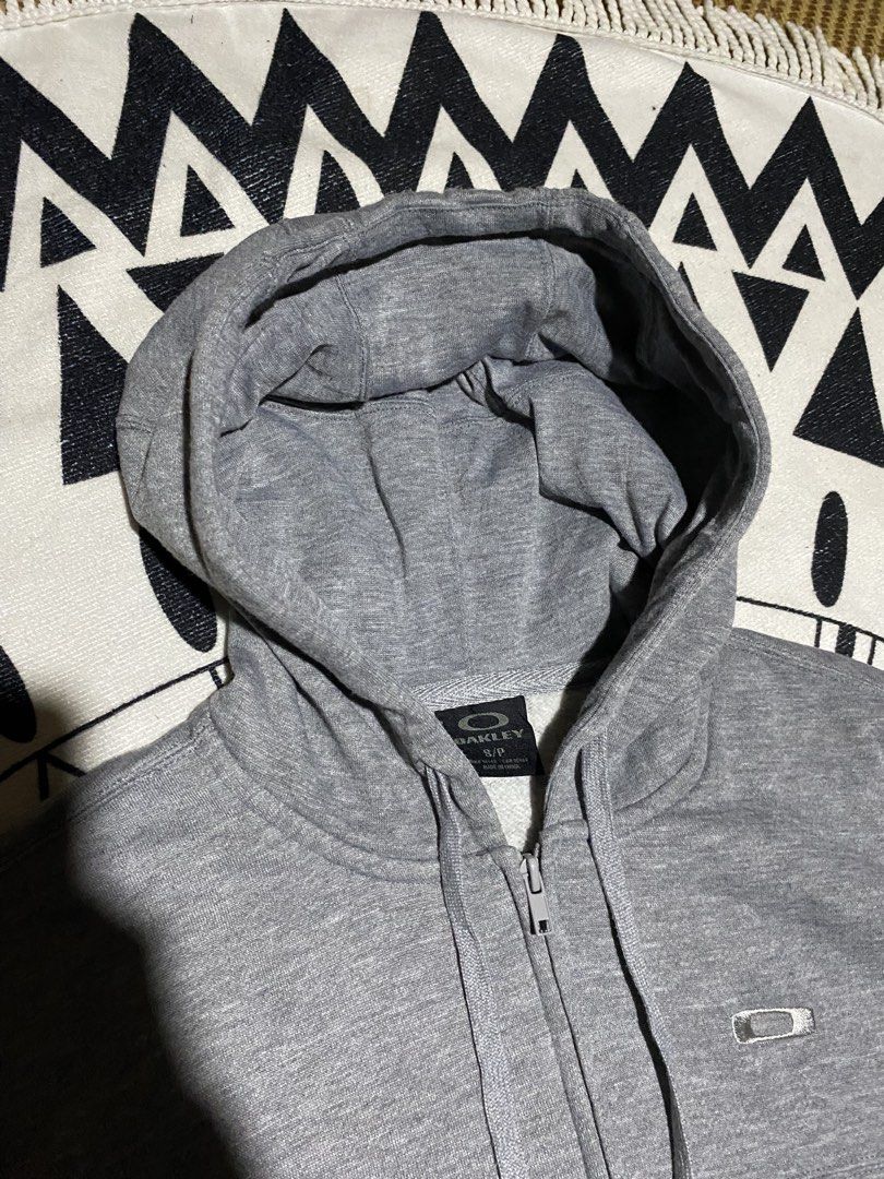 Oakley Grey Zip-Up Hoodie (Category: Coats, Jackets and Outerwear) located in Badiangan. Submitted by iralorana.thrift (Listing ID 1466248238, Image 2). Description: - Brand: Oakley - Style: Grey zip-up hoodie - Size: Small - Features: Full zipper front, matching drawstring hood, two front hand pockets - Special Detail: Ribbed cuffs with thumbholes and small chest logo - Comfort: Soft fleece lining inside for extra warmth - Condition: Excellent, 