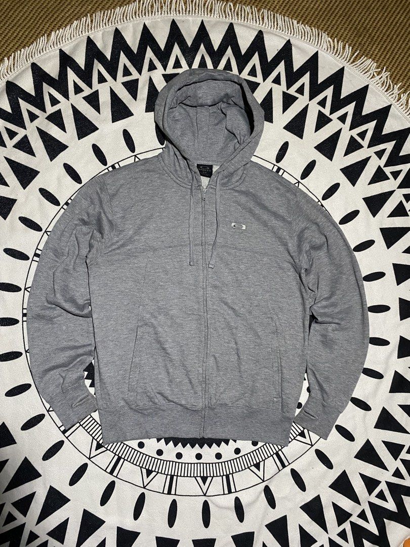 Oakley Grey Zip-Up Hoodie (Category: Coats, Jackets and Outerwear) located in Badiangan. Submitted by iralorana.thrift (Listing ID 1466248238, Image 1). Description: - Brand: Oakley - Style: Grey zip-up hoodie - Size: Small - Features: Full zipper front, matching drawstring hood, two front hand pockets - Special Detail: Ribbed cuffs with thumbholes and small chest logo - Comfort: Soft fleece lining inside for extra warmth - Condition: Excellent, 