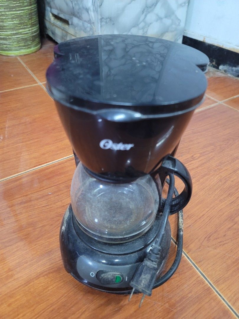 Oster Black Coffee Maker (Category: Coffee Machines & Makers) located in Manila. Submitted by liezle7 (Listing ID 1466335774, Image 1). Description: - Brand: Oster - Type: Drip coffee maker in classic black - Includes: Glass carafe and power cord - Features: Easy on-off switch located on the base - Condition: Pre-loved, needs a good cleaning before use - Note: Coffee maker only (wooden countertop not included).