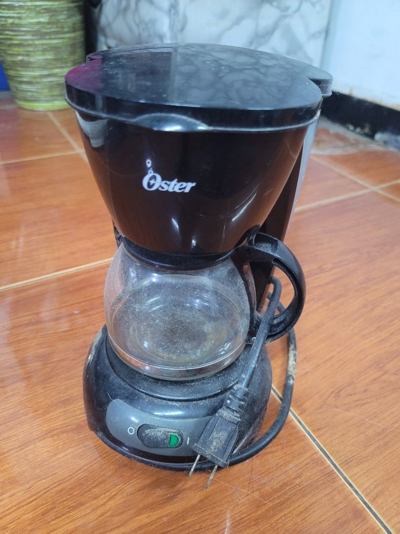 Oster Black Coffee Maker (Category: Coffee Machines & Makers) located in Manila. Submitted by liezle7 (Listing ID 1466335774, Image 2). Description: - Brand: Oster - Type: Drip coffee maker in classic black - Includes: Glass carafe and power cord - Features: Easy on-off switch located on the base - Condition: Pre-loved, needs a good cleaning before use - Note: Coffee maker only (wooden countertop not included).