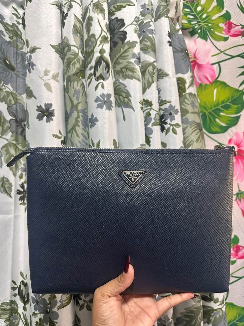 P R A D A (Category: Luxury Bags & Wallets) located in Tambulig. Submitted by cmscloset_ph (Listing ID 1466290216, Image 1). Description: PRADA Saffiano leather clutch in navy blue - Sleek structured shape with silver-tone hardware - Classic triangular metal logo plate on the front - Secure zip top closure with fully lined interior - Medium size: ideal for essentials or as a tote insert.