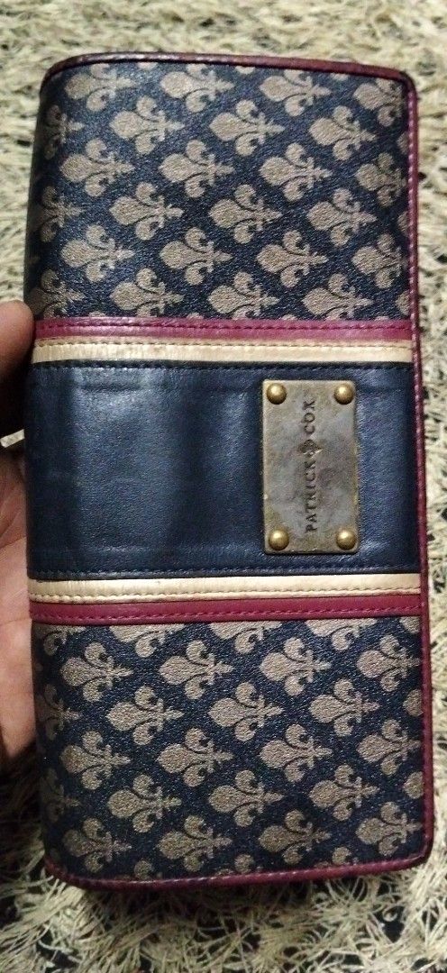 Patrick Cox Fler de Lis Long Wallet (Category: Wallets & Card holders) located in Paranaque City. Submitted by michael-08 (Listing ID 1466191882, Image 2). Description: - Authentic Patrick Cox long wallet - Eye-catching blue and gold fleur-de-lis pattern with dark leather center panel - Metal brand plate accent - Features multiple card slots, cash compartments, and a secure zipped inner pocket - Stylish maroon fabric lining - Convenient side snap