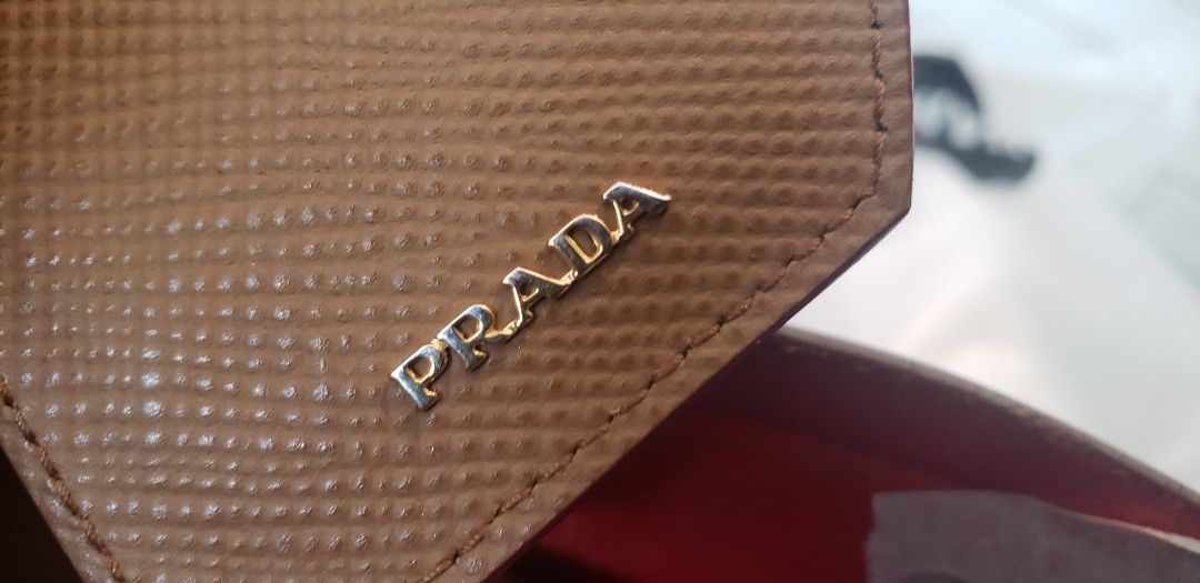 Prada Saffiano Leather Tote Bag (Category: Luxury Bags & Wallets) located in Marikina City. Submitted by racoon143 (Listing ID 1466200454, Image 3). Description: Prada tote bag in light brown Saffiano leather. Gold hardware and metal lettering logo on the front triangular plaque. Double top handles. Red leather interior lining with Prada heatstamp branding. Includes matching leather luggage tag with gold Prada lettering. Clean structure, firm sha