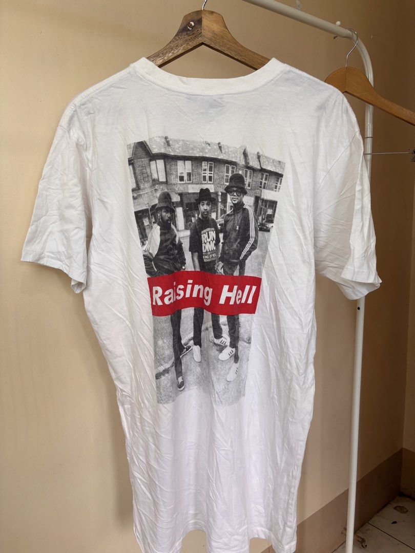 Run DMC Raising Hell White T-Shirt (Category: Tshirts & Polo Shirts ) located in Andop. Submitted by ukaylangpo (Listing ID 1466193439, Image 2). Description: - Item: White Run DMC Graphic Tee - Size: Tagged M/M (Measures approx. 23-24 inches across the chest) - Design: Small red 'Raising Hell' box logo on front, large black & white band photo with 'Raising Hell' banner on back - Fit/Material: Standard fit, comfortable cotton fabric.