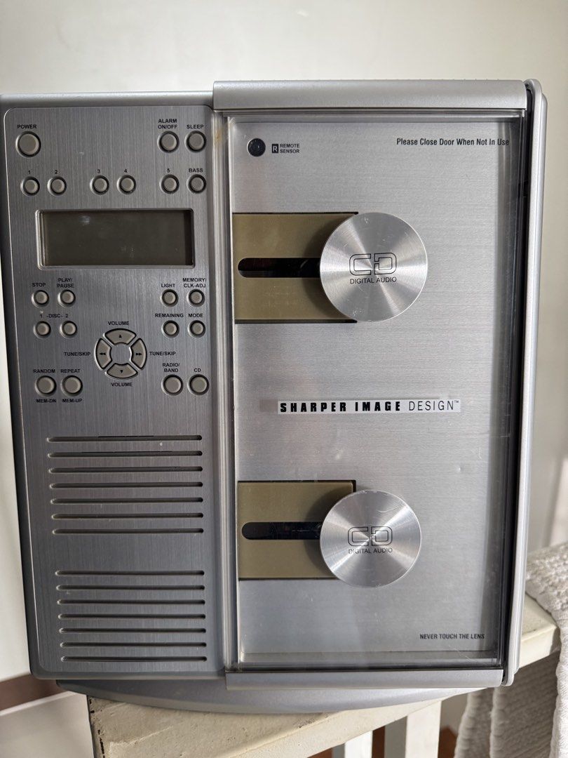 Sharper Image Design CD Digital Audio Player (Category: Portable Music Players) located in Cavite. Submitted by marcuz1316 (Listing ID 1466254404, Image 1). Description: - Brand: Sharper Image Design - Color: Sleek silver finish with round metallic door covers - Design: Vertical dual CD slot setup with a central digital display - Controls: Left-side panel for power, alarm, volume, and playback - Inclusions: Comes with the original remote control 