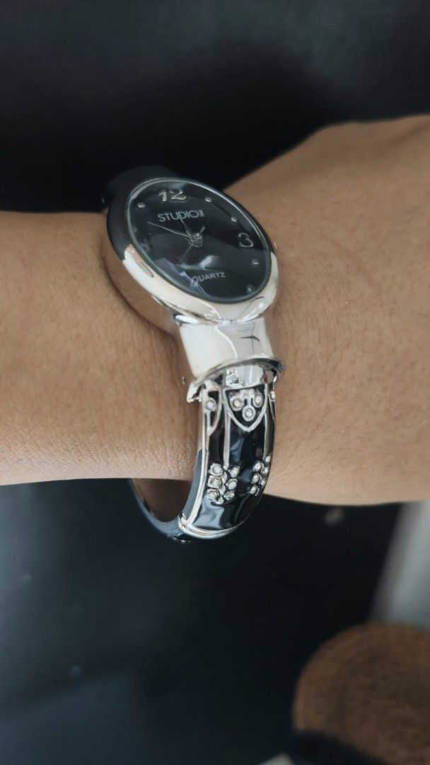 STUDIO Time Quartz Oval Bangle Watch (Category: Women's Watches) located in Taguig. Submitted by mercyeugen28914 (Listing ID 1466287815, Image 3). Description: - Brand/Type: Studio Time quartz watch - Dial: Oval black dial with silver bezel - Band: Black enamel bracelet-style cuff with floral motifs and rhinestone crystals - Design: Easy slip-on bangle - Condition: Keeps good time.