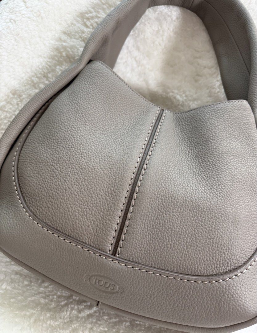 Tod's Grey Leather Hobo Bag (Category: Luxury Bags & Wallets) located in San Juan City. Submitted by jgoods11 (Listing ID 1466160472, Image 1). Description: - Brand: Tod's - Color: Soft Grey - Material: Supple pebbled grain leather with white contrast stitching - Design: Curved hobo silhouette with a thick structured handle and debossed front logo - Condition/Interior: Clean interior lining - Style: Everyday luxury shoulder bag.