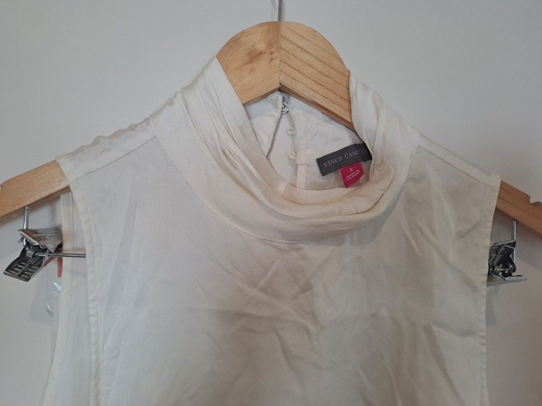 Vince Camuto off white sleeveless (Category: Sleeveless) located in Manila. Submitted by joanbalde39643 (Listing ID 1466255096, Image 2). Description: This is a Vince Camuto sleeveless high-neck blouse in an off-white or new ivory satin/crepe fabric. It features a sophisticated mock turtleneck or funnel neckline with subtle gathering or pleating at the throat and a clean, minimalist silhouette perfect for layering or wearing as a chic standalone 