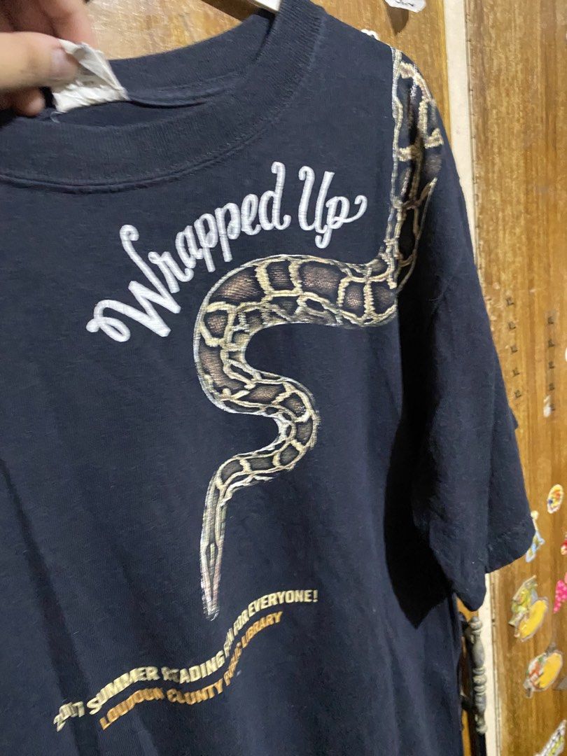 Vintage Anvil Wrapped Up Snake Graphic Tee (Category: Tshirts & Polo Shirts ) located in Imus. Submitted by frootiloots4103 (Listing ID 1466208019, Image 2). Description: - Brand/Style: Black Anvil t-shirt from the 2017 Loudoun County Public Library summer reading program - Graphics: 'Wrapped Up' text on front, 'In Reading' on back, featuring a large python snake graphic wrapping around the shoulder and down both sides - Details: Corporate sponso