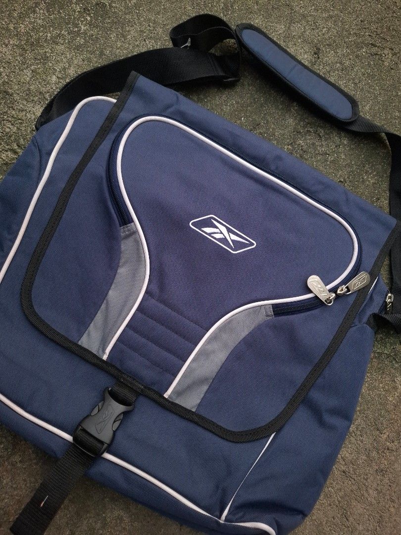 Vintage Reebok Messenger Bag Blue (Category: Sling Bags) located in Manila. Submitted by bonaobrag55538 (Listing ID 1466200538, Image 3). Description: Blue Reebok messenger bag with grey piping details and white embroidered logo. Front flap pocket with dual zippers, main compartment with inner dividers and Velcro strap. Adjustable shoulder strap featuring a padded section for comfort. Sturdy plastic buckle closure on the front flap..