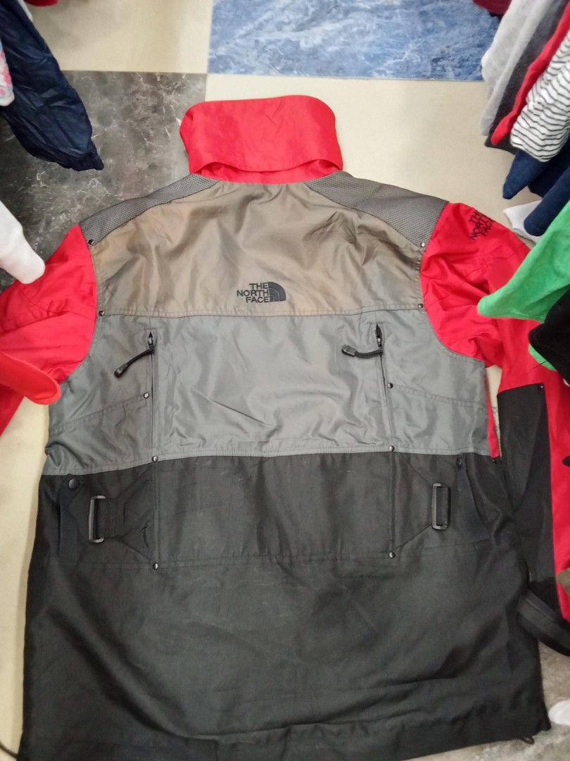 Vintage The North Face Steep Tech Red Black Jacket (Category: Coats, Jackets and Outerwear) located in Bogo. Submitted by thrift_kier (Listing ID 1466314750, Image 2). Description: - Brand: The North Face Steep Tech (Designed by Scot Schmid) - Size: Men's Large - Colorway: Red, grey, and black - Design: Heavy pocket detailing on the front with utility straps - Features: Multiple zip pockets and adjustable cuffs - Branding: Iconic branding on the 