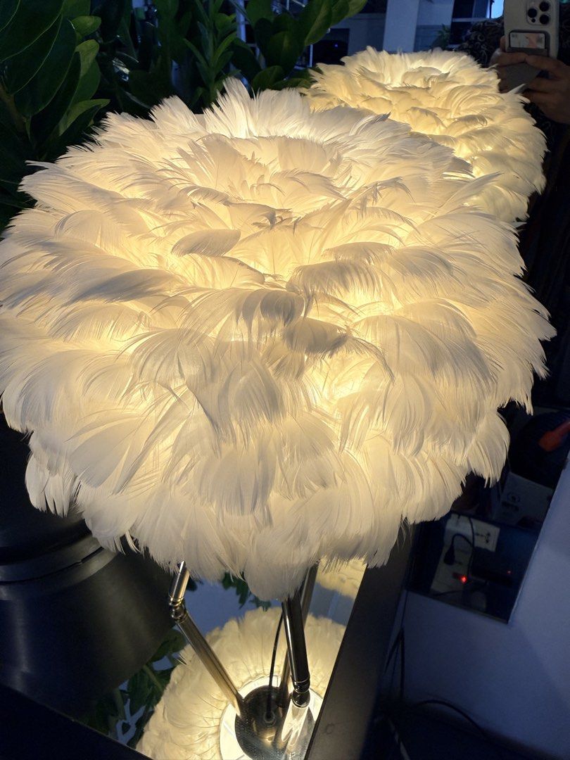 White Feather Shade Table Lamp with Gold Legs (Category: Lighting) located in Quezon City. Submitted by yourheaduhunter (Listing ID 1466225640, Image 3). Description: - Fluffy white feather lampshade for a chic, aesthetic look - Slender gold-toned metal tripod stand for stability and style - Emits a cozy warm yellow glow when lit up - Perfect statement piece for bedside tables or living room corners.